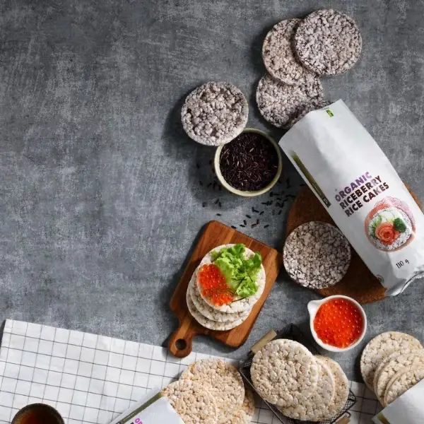 Assorted organic rice cakes with packaging and toppings on a gray background